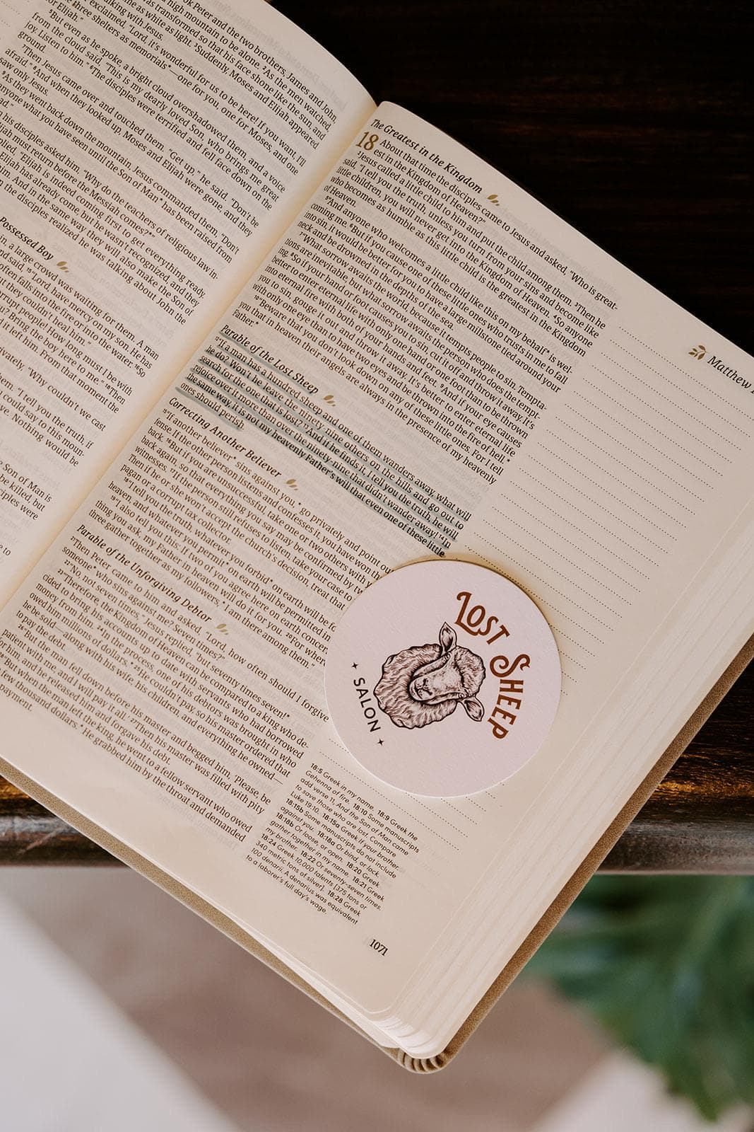 A Lost Sheep Salon sticker resting on an open Bible at the Parable of the Lost Sheep