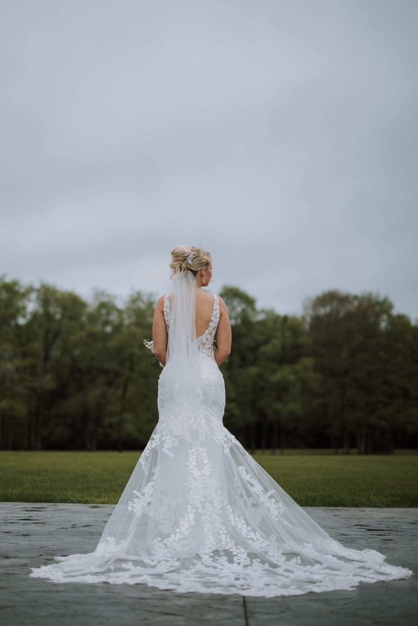 Bride from behind in a lace mermaid gown with a cathedral train spread across the courtyard, photo by Kirkland Photography