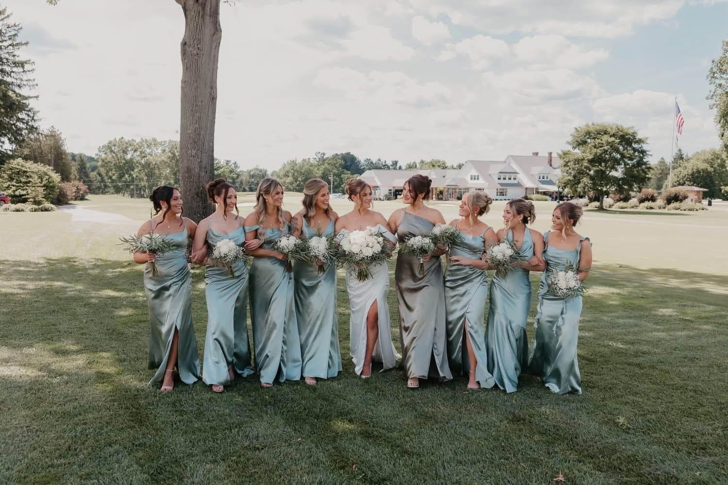 Bride and her bridesmaids in sage-green gowns with bridal updos, styled by Lost Sheep Salon on the wedding lawn